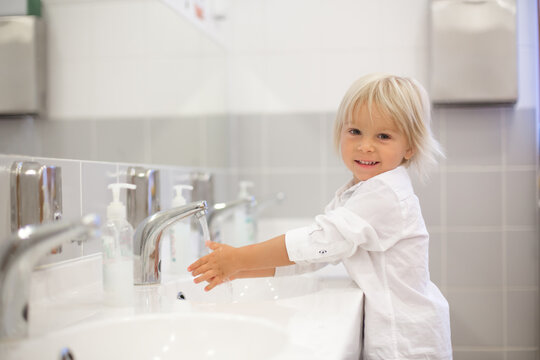 Little preschool child, blond boy, washing hands in bathroom in kindergarden