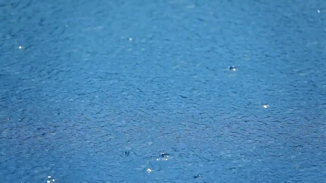 Sparkling ripples and water crown  on blue water surface .
Close up  of  rain drops fallng into blue water  of swimming pool  in slow motion,HD video.
Abstract ripples background.
