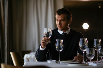 Handsome businessman dressed in the suit drinking wine. Businessman enjoying in the restaurant..