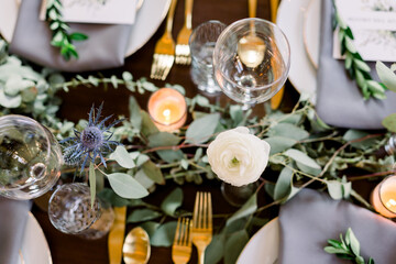 Fototapeta na wymiar Top down view of a table with beautiful roses, eucalyptus leaves, and a greenery garland on a table set with empty wine glasses and gold silverware. 
