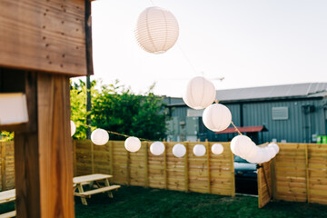 White Paper Lanterns  hung up in a backyard with a wood fence. 