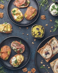 Assorted bruschetta with various toppings on a dark plates on dark background. Appetizing bruschetta. Mediterranean cuisine. Top view