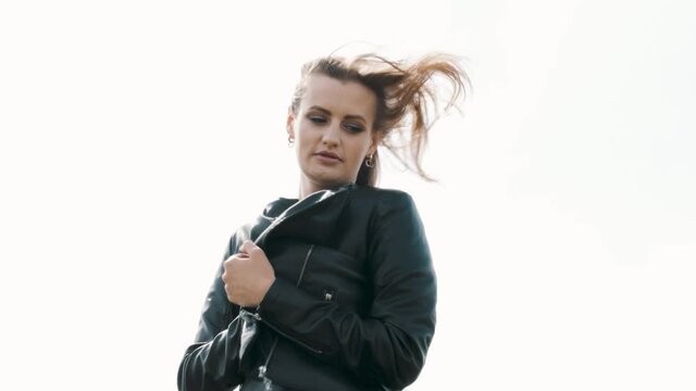 Confident elegant woman in Leather Jacket standing on white background, female brown hair blowing in wind. Feeling of freedom and independence. Feminists