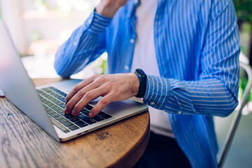 Crop man typing on netbook keyboard in summer area of cafe