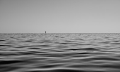 black and white seascape of calm sea with sails boat in the background - peace and relax concept.