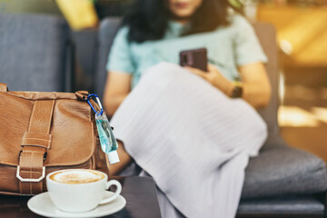 Mini alcohol gel bottle to kill Corona Virus(Covid-19) hang on a brown leather shoulder bag with hot coffee on table in cafe.New normal lifestyle.Health care concept.Selective focus on alcohol gel
