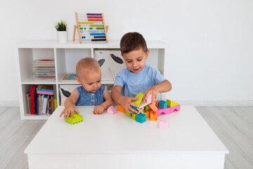 boy and little rirl sit at a table and play with a colorful wooden bloks