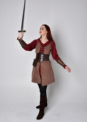 Full length portrait of girl wearing medieval costume. Standing pose holding a sword,  isolated against a grey studio background.