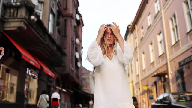 Attractive young lady walking on city street, she turns to camera and smiles. Outdoor portrait happy female tourist having good time wandering around town in summer