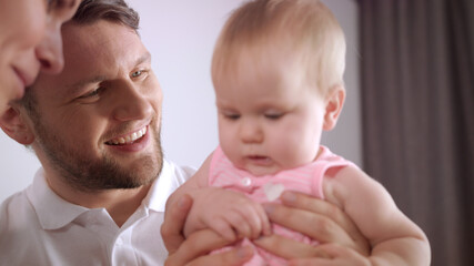 Adorable baby girl in father embrace. Portrait of infant play with mom and dad