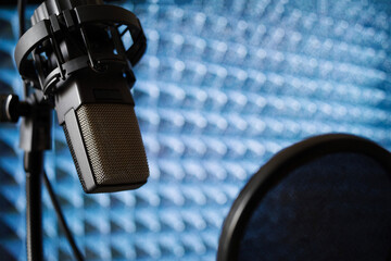 Microphone in recording studio with pop filter on acoustic foam panel background, close up, soft focus