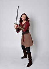 Full length portrait of girl wearing medieval costume. Standing pose holding a sword,  isolated against a grey studio background.