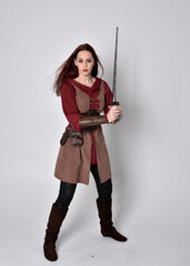 Full length portrait of girl wearing medieval costume. Standing pose holding a sword,  isolated against a grey studio background.