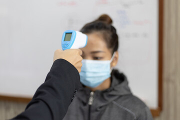 Asian teacher checking female student's temperature.