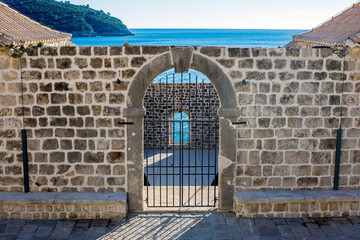 Closed bar door with shadows, selective focus, blue Adriatic Sea behind, sunny day. Scenery winter view of Mediterranean old city of Dubrovnik, famous European travel and historic destination, Croatia