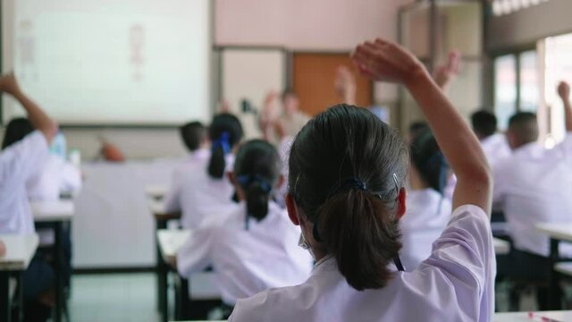 Slow motion of Asian high school students in white uniform actively study science by raising their hands to answer questions on projector screen that teachers ask them  in science classroom.