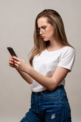 Fototapeta premium Social media anxiety. Disturbing news. Concerned woman in glasses reading feed on phone isolated on gray background. Mobile technology. Internet stress.