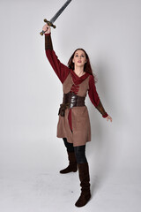 Full length portrait of girl wearing medieval costume. Standing pose holding a sword,  isolated against a grey studio background.