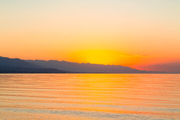 Dawn of the sun at sea. The rising sun behind the mountains. Kyrgyzstan.