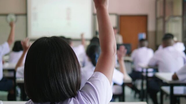 Slow motion of Asian high school students in white uniform actively study science by raising their hands to answer questions on projector screen that teachers ask them  in science classroom.