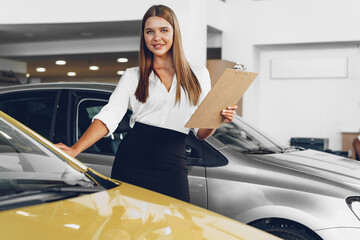 Attractive young female car dealer standing in showroom