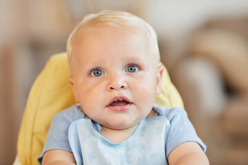 Close-up portrait of cute little child sitting on high chair waiting for food looking at camera,...