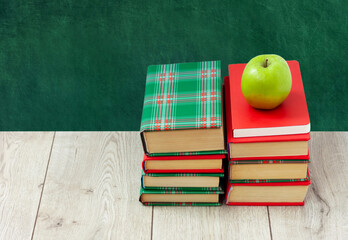 Back to school, pile of books in colorful covers and green apple on wooden table with empty green school board background. Distance home education. Quarantine concept of stay home.