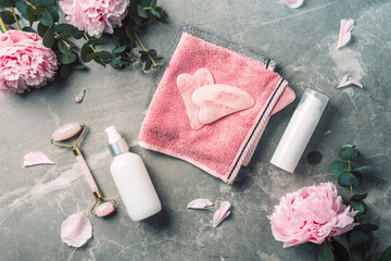 Fototapeta na wymiar Facial roller, gua sha massager, oil bottle, towel, pink peonies on marble background. Copy space. Flat lay. Top view. Routine facial skin care, body treatment, spa concept.