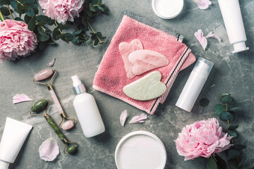 Obraz na płótnie Canvas Cosmetic products bottles, towels, oil, face roller and gua sha massager, pink peonies flowers on marble background. Banner. Top view. Spa relax, body treatment, spa, skin care concept