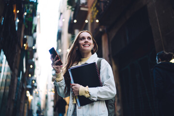 Cheerful modern female student texting on street