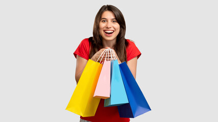 Holiday gifts. Shopaholic lifestyle. Excited woman holding colorful bags looking at camera isolated on neutral copy space. Sale and discount. Black friday. Cyber monday