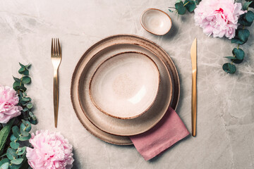 Tableware, flowers for serving a festive table, dinner. Stoneware plates, golden cutlery, eucalyptus branches, peony flowers on marble background. Copy space. Flat lay, top view. Table setting