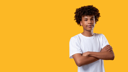 Black teenager. Social tolerance. Smiling african young male crossing arms looking at camera isolated on orange copy space. Confident pose. Disapproving emotion. No racism - obrazy, fototapety, plakaty