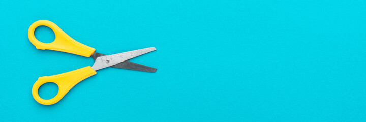 Minimalist photo of yellow children's scissors on the turquoise blue background. Flat lay shot of opened yellow scissors with copy space.