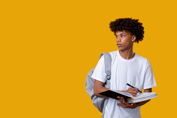 Smart black teenager. Student lifestyle. Young african male writing in notebook isolated on orange...