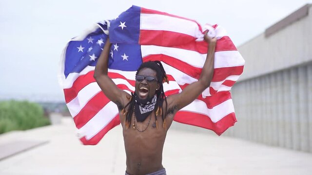 Dark-skinned male protester waves an American flag in the street, Slow motion. No racism.