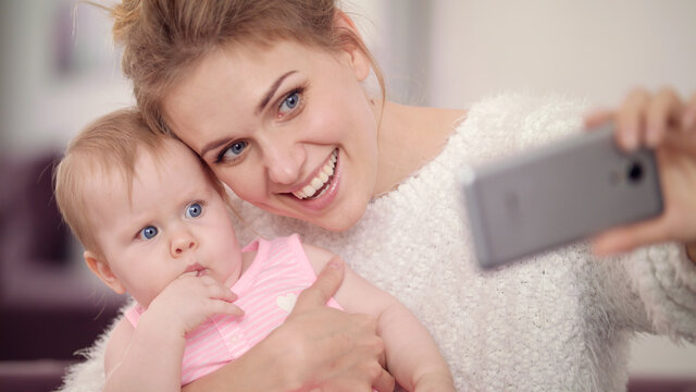 Smiling mother making selfie photo with baby girl. Woman with kid mobile photo