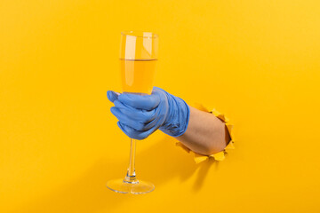 Hand in a latex glove holding a glass of champagne through torn yellow wall