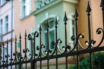 black metal fence with peaks in perspective of a garden with an colorful house and bush.