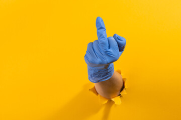 Hand in a latex glove showing middle finger through torn yellow wall