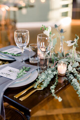 Beautiful green table scape at a wedding reception with dried eucalyptus leaves and wildflowers in tiny vases and wine glasses on a table.  