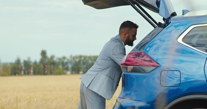 Businessman putting his sport bag into car trunk and closing it by pushing the button, countryside shot