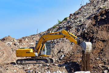 Yellow excavator at landfill for disposal of construction waste. Backhoe dig gravel at mining...