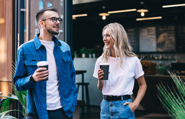 Happy positive woman and man friends enjoying spending time together talking with coffee to go cup, cheerful positive male and female hipsters in trendy casual wear joking and having fun on date