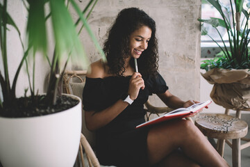 Side view of prosperous female writer creating blog publication sitting with education notebook in...