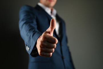 The man shows his thumb forward. A man in a suit shows a big forward on a black background. Concept: a positive message in business.