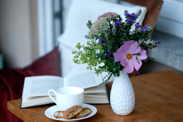 Entspannung und Kaffeepause zuhause auf Balkon mit Kaffeetasse, Buch, Gebäck, Blumenstrauss, Tisch.
