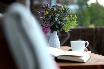 Entspannung, Urlaub, Pause zuhause auf Balkon mit Kaffeetasse, Buch, Gebäck, Blumenstrauss.