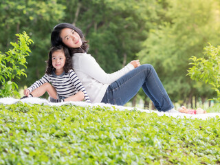 Asian little girl sitting with her mom on the carpet, Relax and learning outside of school to enjoy in the nature park