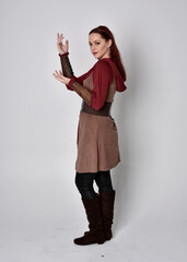 Full length portrait of girl wearing medieval costume. Standing pose with back to the camera,  isolated against a grey studio background.